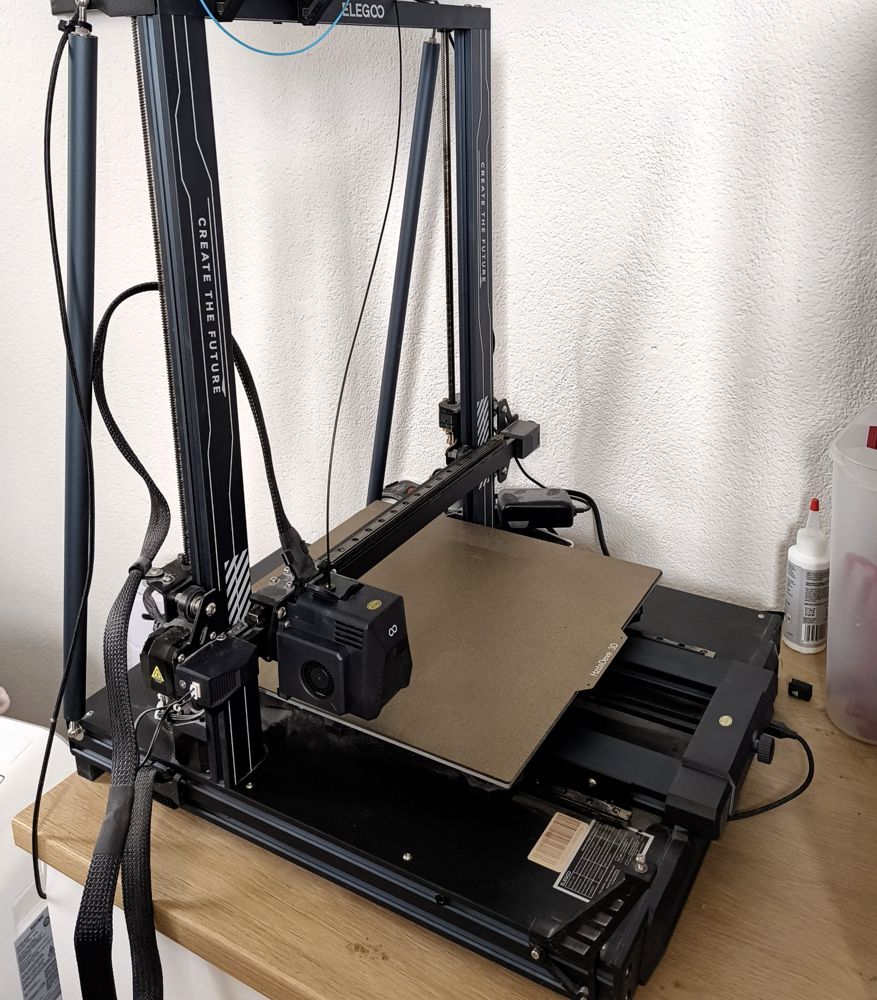Offener Portaldrucker Neptune 3 Plus mit großem Druckbett auf einer Holzplatte.