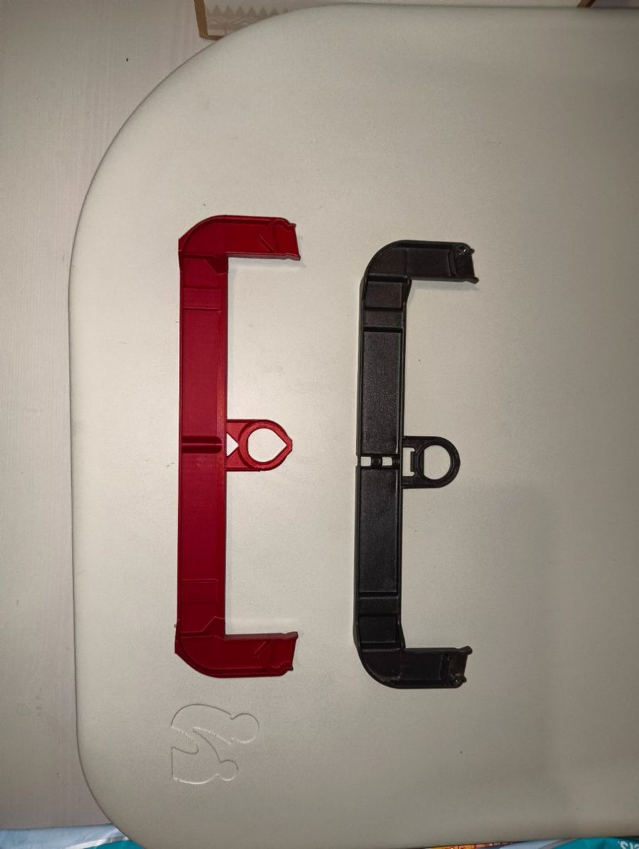 Zwei gleich geformte Kunststoffbügel nebeneinander: links der rot gedruckte Nachbau, rechts das schwarze Original.